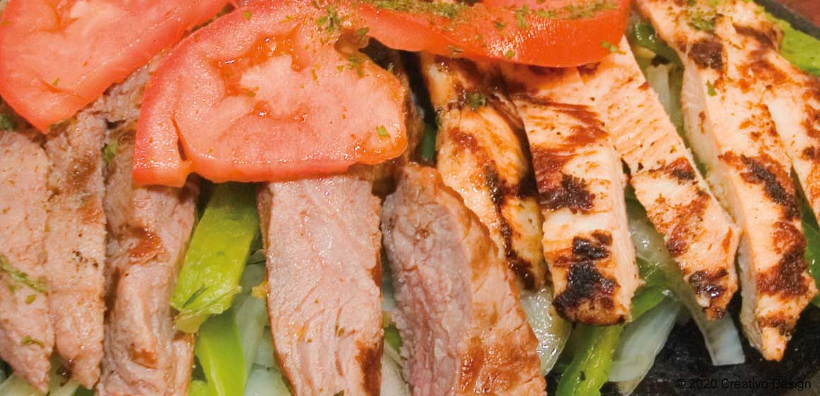 Sizzling grilled steak and chicken fajitas with peppers and tomatoes